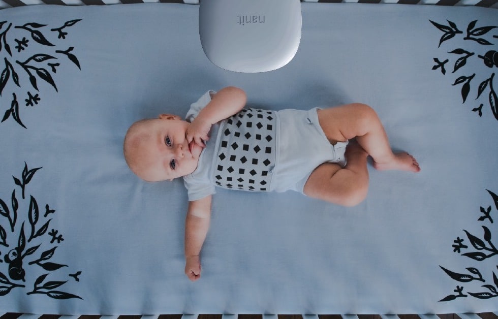 Logicbroker + Nanit Success Story Hero Image; Image of infant lying down wearing a Nanit smart baby monitor